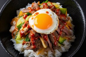 Colorful Korean bibimbap bowl with rice, sautéed vegetables, a fried egg, and gochujang sauce.