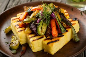 Grilled polenta slices served with a colorful mix of roasted vegetables.